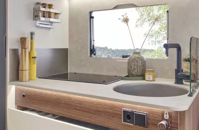 Cuisine compacte de camping-car avec évier, plaques de cuisson et rangements ouverts.
