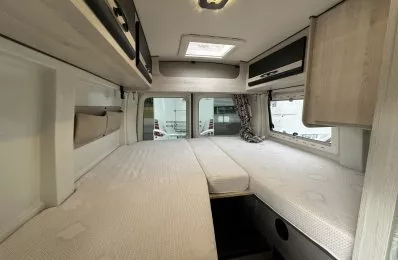 Intérieur d'un camping-car avec lits jumeaux et rangements en bois clair.