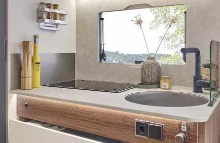 Cuisine compacte de camping-car avec évier, plaques de cuisson et rangements ouverts.