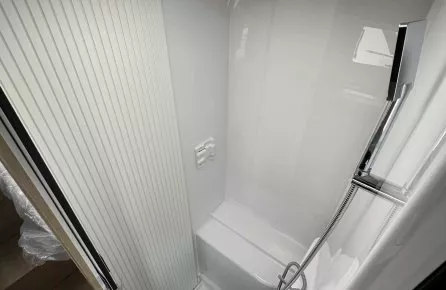 Douche compacte avec parois blanches et pommeau, dans un espace restreint de véhicule récréatif.