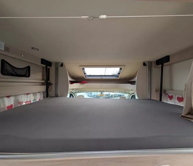 Intérieur d'un camping-car avec lit surélevé et hublot de toit.