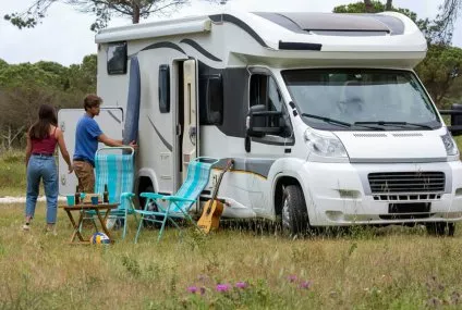 Camping-car stationné dans un champ avec deux personnes et des chaises pliantes.