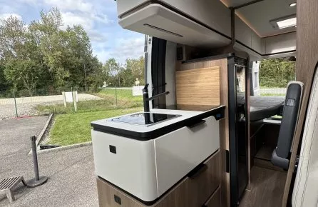 Intérieur moderne d'un camping-car avec cuisine équipée et vue sur l'extérieur verdoyant.