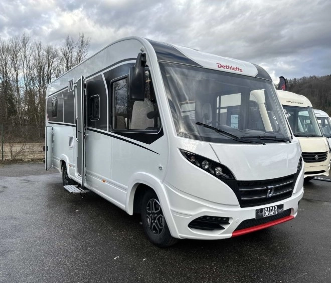 Camping-car Dethleffs blanc stationné sur un parking, ciel nuageux en arrière-plan.