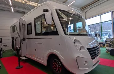 Camping-car blanc exposé dans un showroom lumineux avec sol rouge et vert.