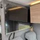 Intérieur d'un camping-car avec placards en bois et revêtement en tissu gris.