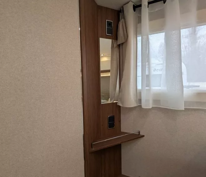 Intérieur d'une caravane avec étagères en bois et fenêtre avec rideaux blancs.