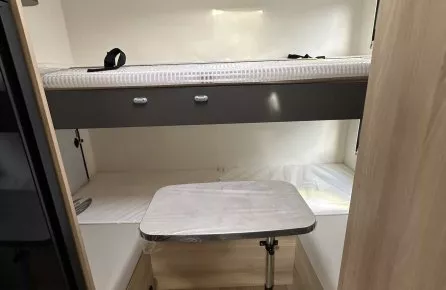 Intérieur d'un camping-car avec lits superposés et table pliante en bois clair.