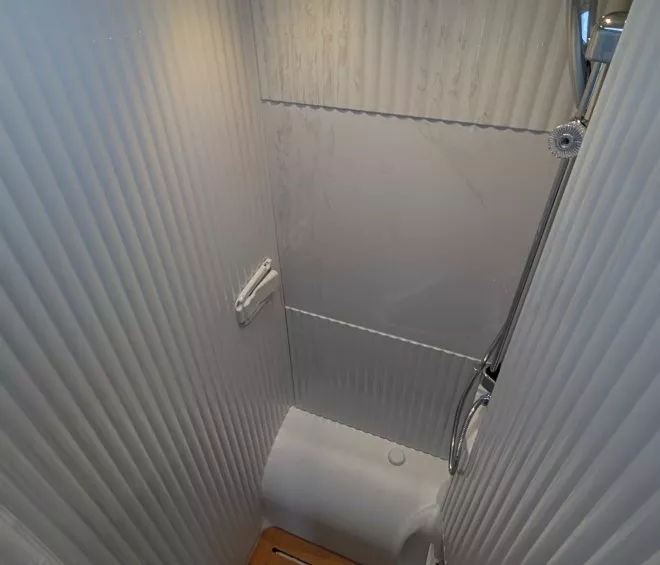 Douche compacte avec parois blanches et caillebotis en bois, éclairage intégré.