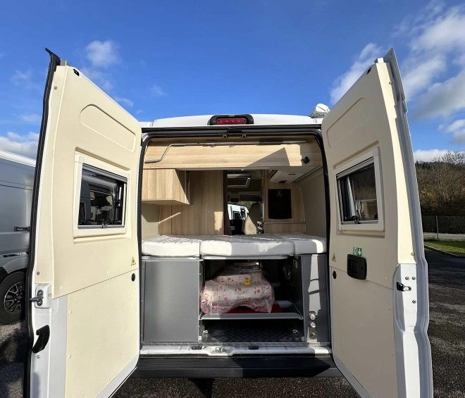 Intérieur d'un van aménagé avec portes arrière ouvertes sous un ciel bleu.