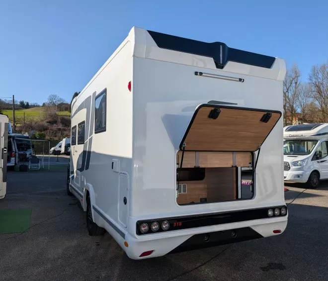 Camping-car blanc avec coffre arrière ouvert sur un parking ensoleillé