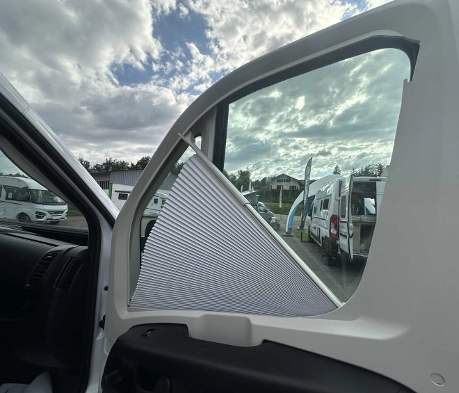 Vue intérieure d'un véhicule avec store plissé, camping-cars en arrière-plan