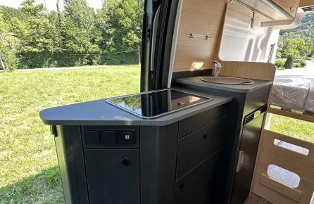Intérieur d'un camping-car moderne avec cuisine équipée, vue sur l'extérieur verdoyant.