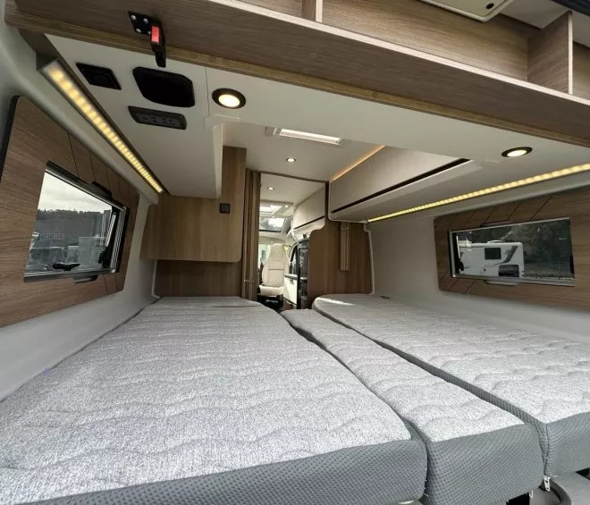 Intérieur d'un camping-car avec lits jumeaux et finitions en bois moderne.