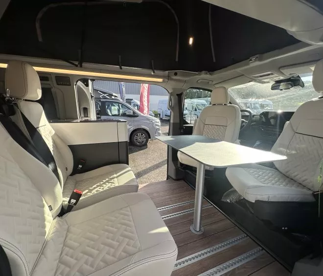 Intérieur d'un van aménagé avec sièges en cuir et table pliante, idéal pour le camping.