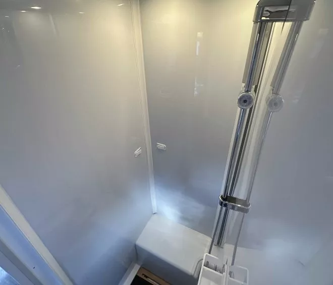 Douche moderne avec parois blanches et éclairage intégré, équipée d'une colonne de douche chromée.