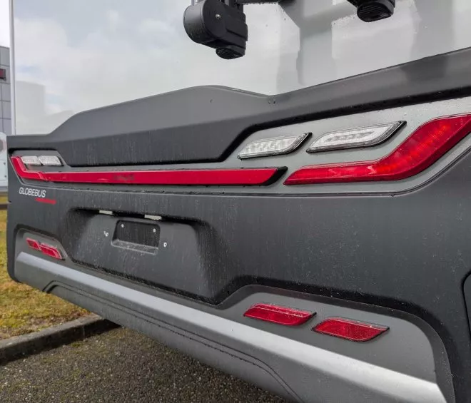Vue arrière d'un camping-car GlobeBus avec feux arrière allumés, stationné sur un parking.