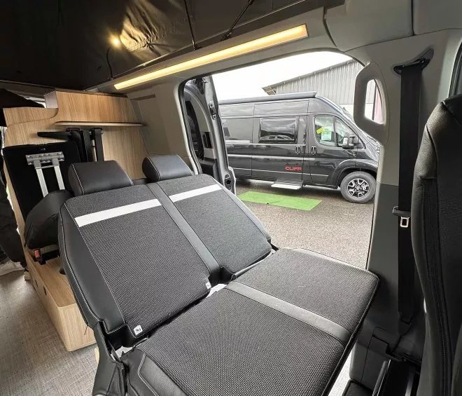 Intérieur d'un van aménagé avec banquette convertible et espace de rangement en bois.