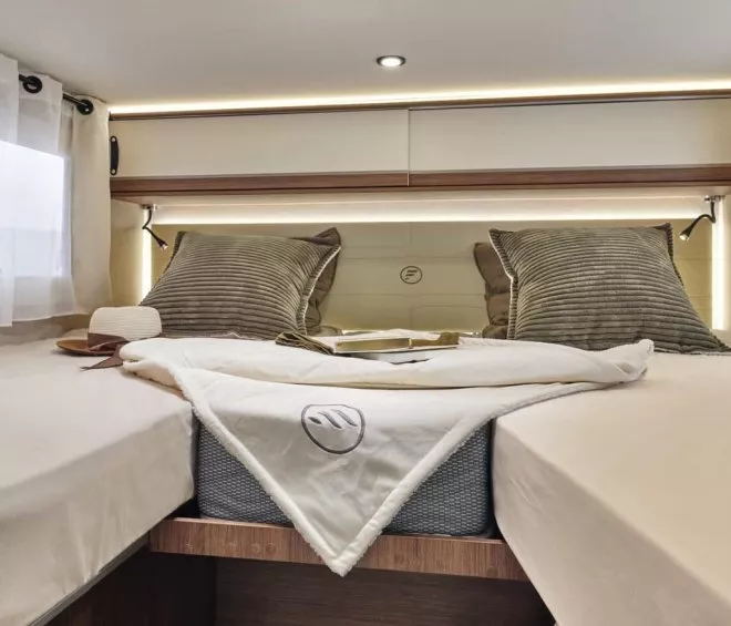 Intérieur d'un camping-car avec lit double, oreillers et lumière douce.