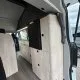 Intérieur d'un van aménagé avec meubles en bois clair et espace de rangement.