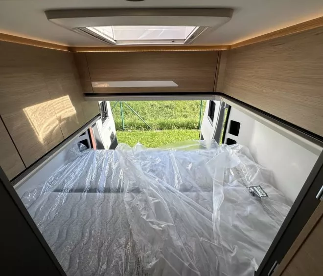 Intérieur d'un camping-car avec lit double et placards en bois clair.