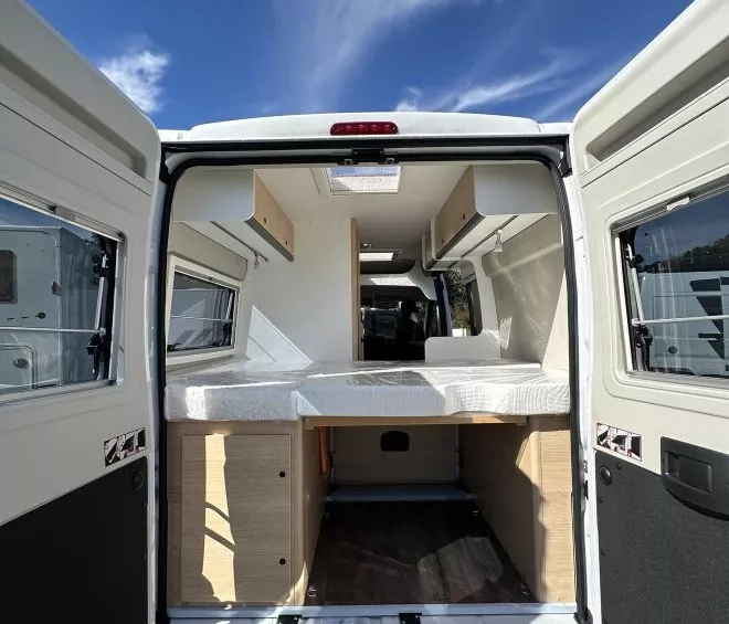 Intérieur d'un van aménagé avec lit et rangements sous un ciel bleu