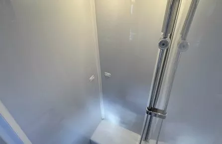 Douche moderne avec parois blanches et éclairage intégré, équipée d'une colonne de douche chromée.