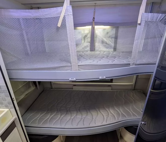 Lits superposés dans un camping-car moderne avec matelas et filets de sécurité.