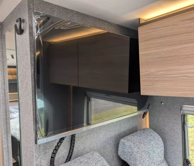 Intérieur d'un camping-car avec placards en bois et revêtement en tissu gris.