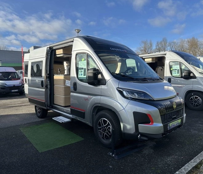 Camping-car gris avec porte latérale ouverte sur un parking