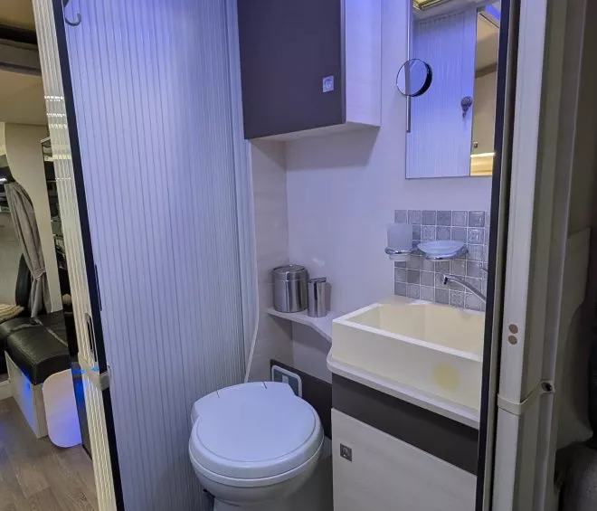 Salle de bain compacte dans un camping-car avec toilettes et lavabo modernes.