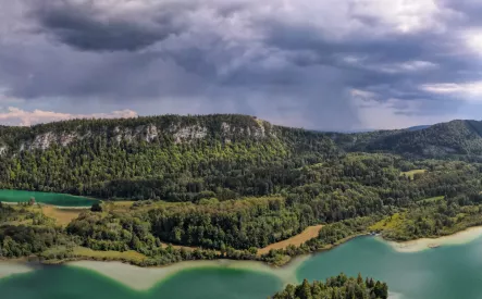 Paysage de lac entouré de forêts sous un ciel nuageux, région montagneuse.