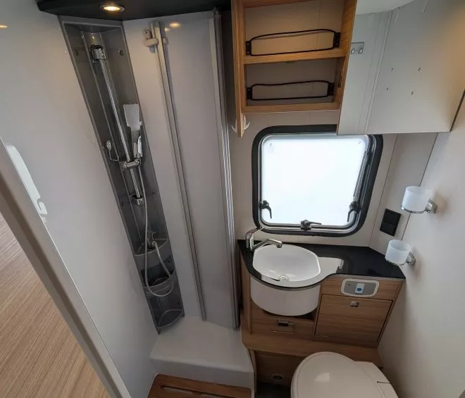 Salle de bain compacte avec douche, lavabo et toilettes dans un camping-car moderne.