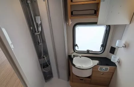 Salle de bain compacte avec douche, lavabo et toilettes dans un camping-car moderne.