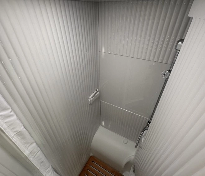 Douche compacte avec parois blanches et sol en bois, éclairage zénithal.