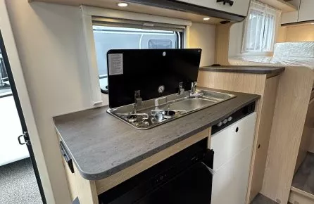 Cuisine compacte de camping-car avec évier, réfrigérateur et rangements.