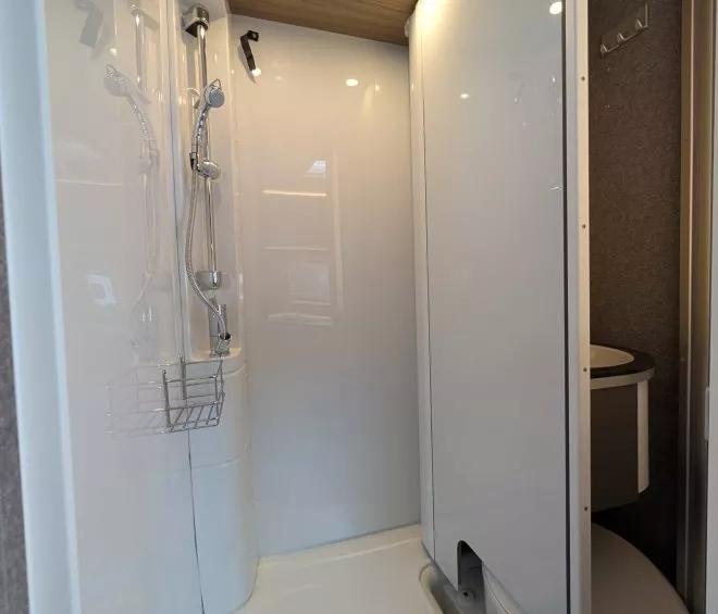 Douche moderne avec parois blanches et éclairage intégré dans un espace restreint.