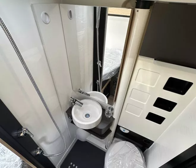 Salle de bain compacte avec douche, lavabo et toilettes dans un camping-car moderne.