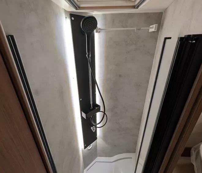 Douche compacte avec pommeau et parois modernes dans un camping-car.
