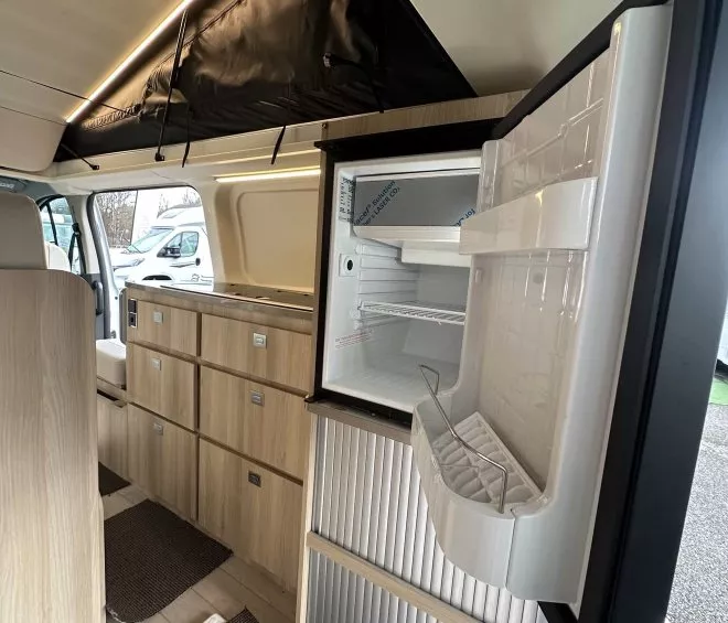 Intérieur d'un van aménagé avec réfrigérateur ouvert et rangements en bois clair.