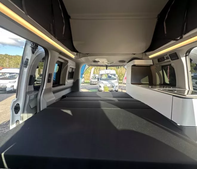 Intérieur aménagé d'un van avec lit et cuisine, stationné en extérieur