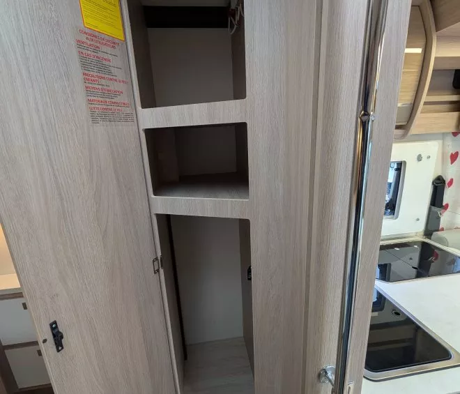 Placard en bois ouvert dans une cuisine de camping-car moderne, avec étagères vides.