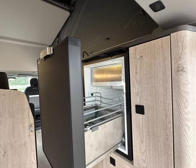 Intérieur d'un van aménagé avec réfrigérateur intégré et placards en bois clair.