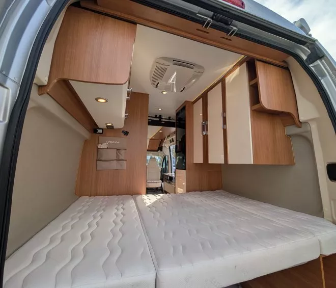Intérieur d'un van aménagé avec lit et rangements en bois clair.