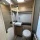Salle de bain compacte en bois clair avec lavabo et toilettes dans un camping-car moderne.