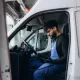 Technicien en bleu de travail dans un véhicule utilitaire, vérifiant un appareil électronique.
