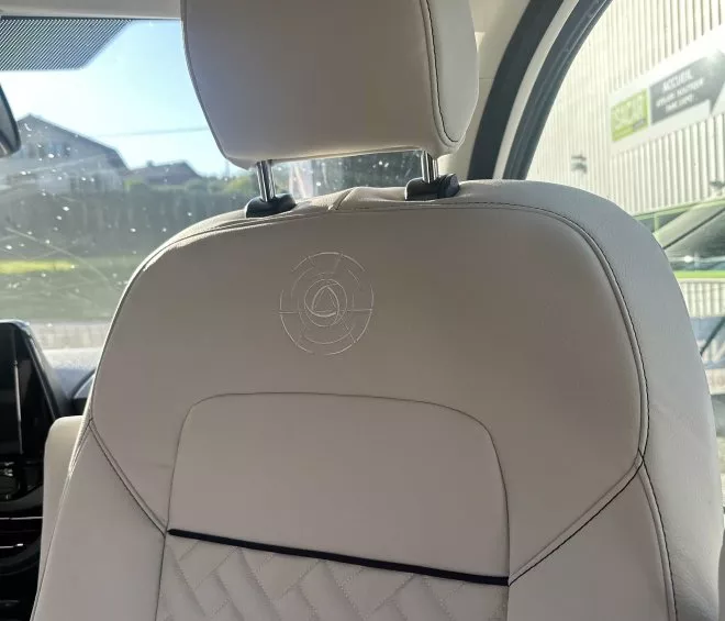 Siège de voiture en cuir beige avec motif tressé et logo brodé, intérieur moderne.