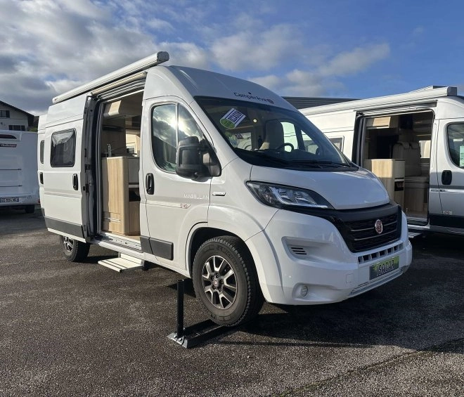 Camping-car blanc stationné avec porte ouverte, ciel nuageux