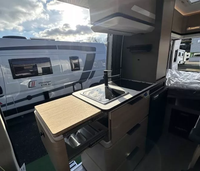 Intérieur d'un camping-car avec cuisine équipée et vue sur un autre véhicule stationné.
