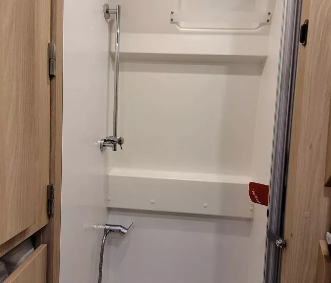 Douche compacte avec parois blanches et porte en bois, équipée d'une pomme de douche et d'un robinet.